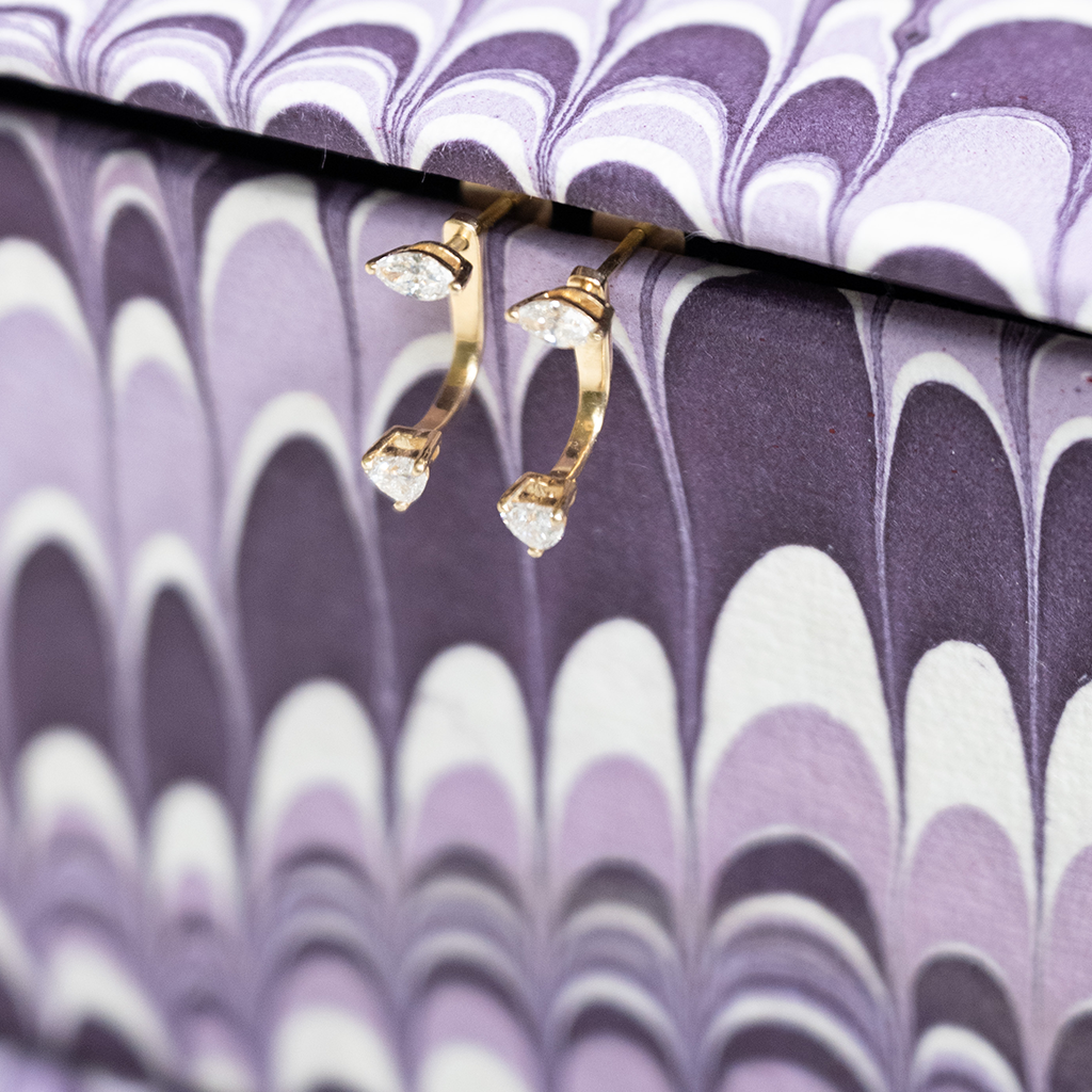 Gold hoop earrings with clear gemstones on a purple and white patterned surface