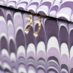 Gold hoop earrings with clear gemstones on a purple and white patterned surface