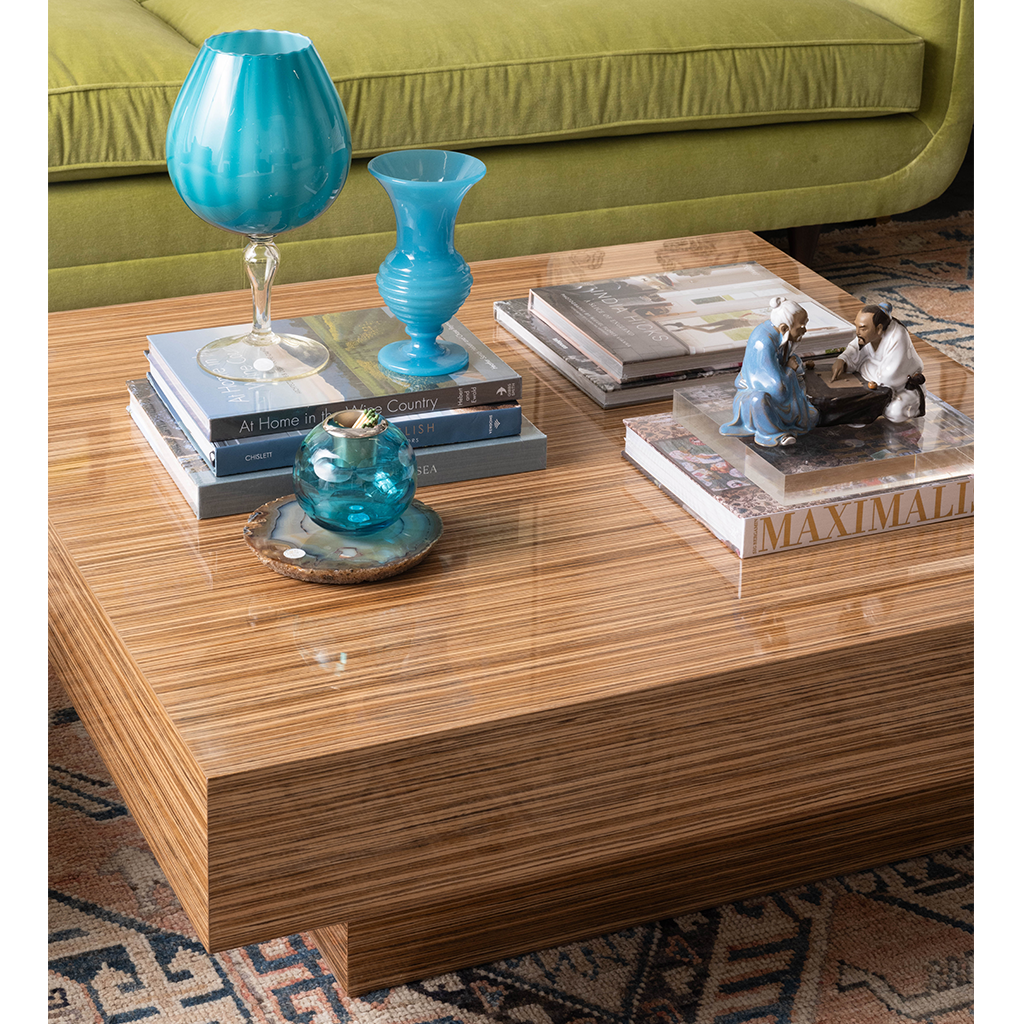 Rectangular wooden cocktail table with a high-gloss finish and striped grain pattern, decorated with blue glass vases and.