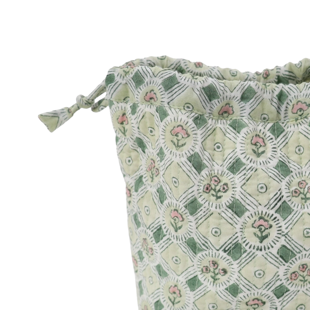 A close-up of a drawstring pouch made of light sage green fabric with a white geometric lattice pattern and small pink floral motifs, shown on a plain white background.
