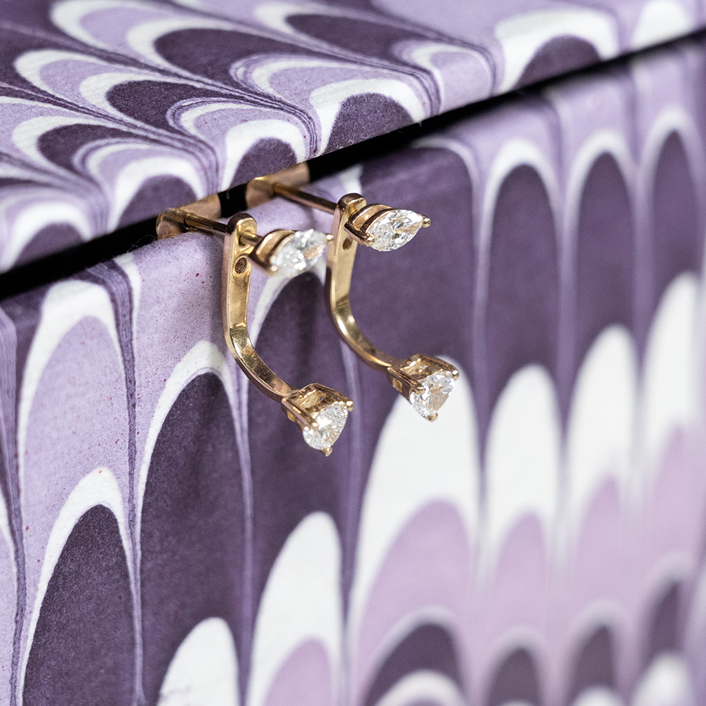 Gold earring with clear stones on a purple and white marbled background