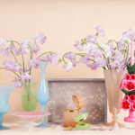 Tall opaline glass vase with a soft purple hue, filled with delicate light pink flowers.