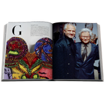 An open book showing a two-page spread with a large decorative mask made of colorful beads on the left page and a color photograph of two men on the right page, photographed against a plain white background.