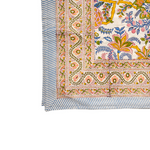 A close-up of a tablecloth corner with a vibrant, multicolored floral and paisley block print on a white base. The pattern features prominent yellow, pink, blue, and green motifs.