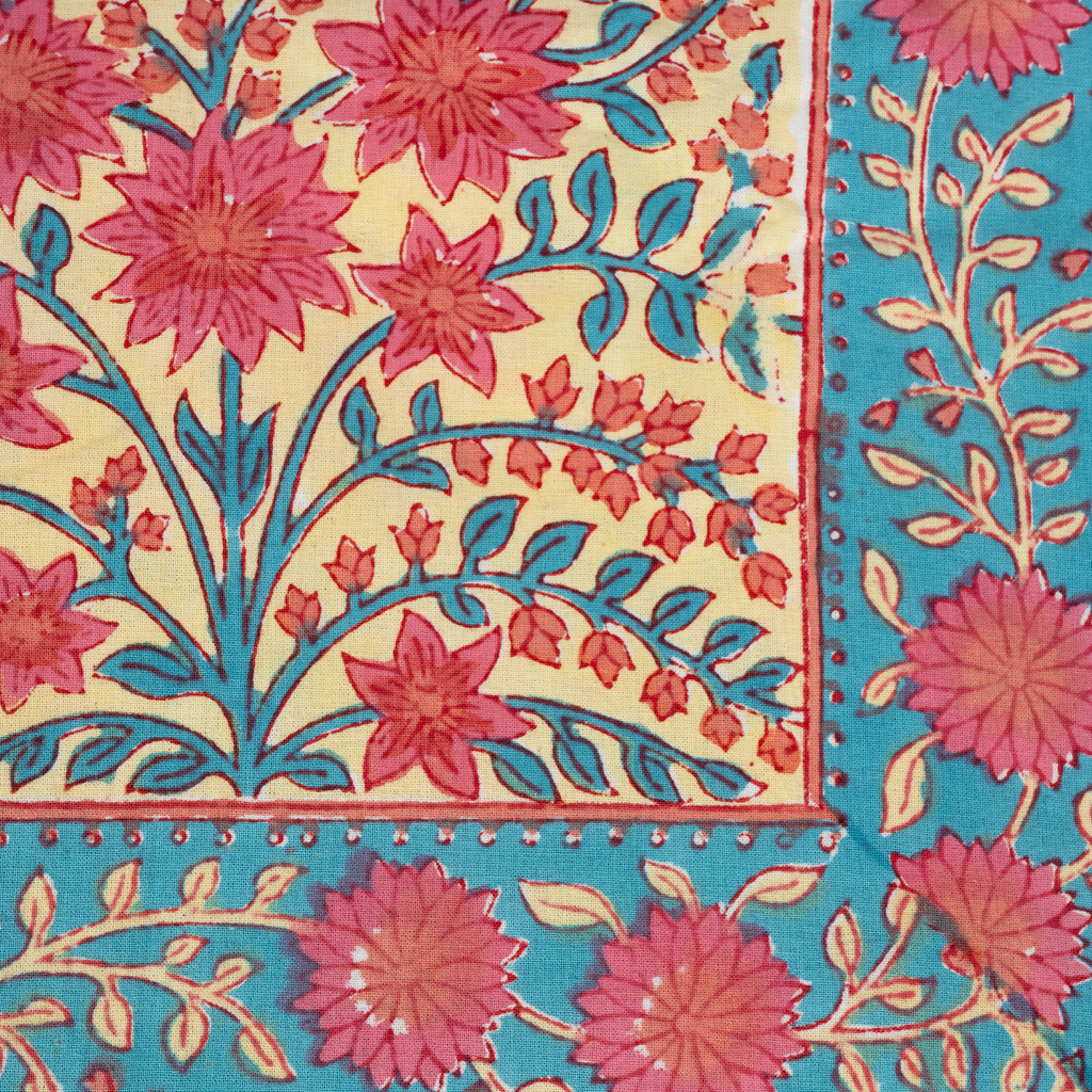 Colorful tablecloth with red floral patterns and blue leafy accents on cream and turquoise background.