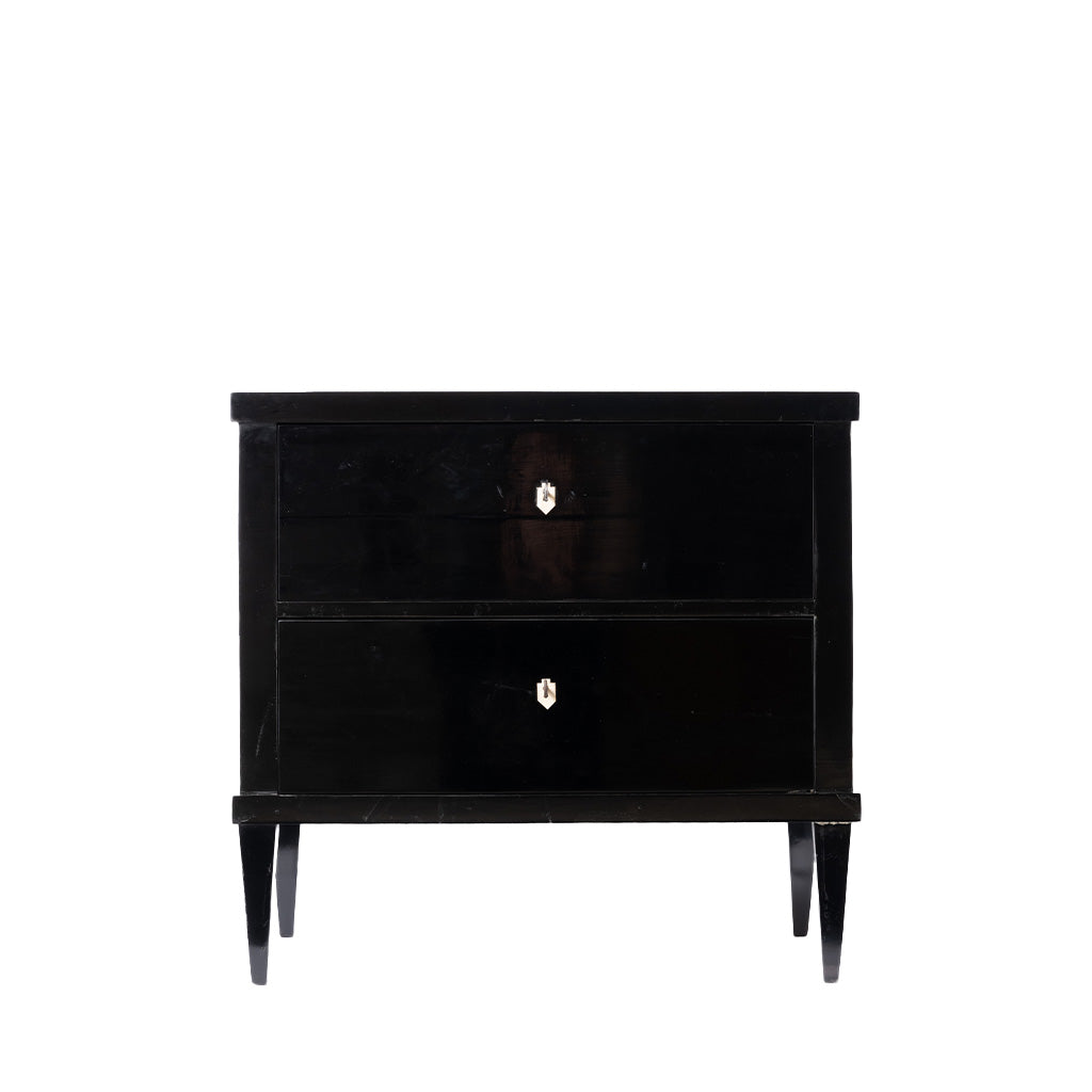 Front view of an antique ebonized two-drawer chest with a glossy black finish, clean lines, and tapered legs. Ivory-colored shield-shaped keyhole escutcheons provide a subtle contrast, emphasizing the piece's refined Biedermeier design.