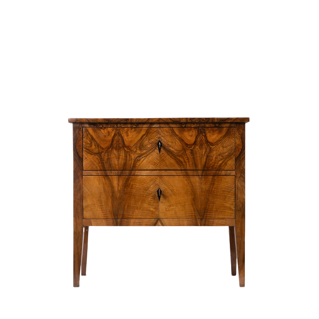 A vintage wooden nightstand featuring a rich, wavy grain pattern on its two drawers, with small dark metal key handles and tapered legs, shown against a plain white background.