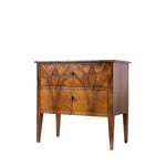 A vintage wooden nightstand with two drawers, featuring a richly figured brown and golden-brown wood grain pattern, tapered legs, and small dark metal key handles, shown against a plain white background.