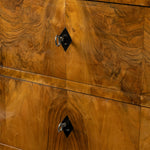 Close-up of a polished wood cabinet or dresser with dramatic swirling grain, black diamond-shaped drawer pulls, and silver ring handles.