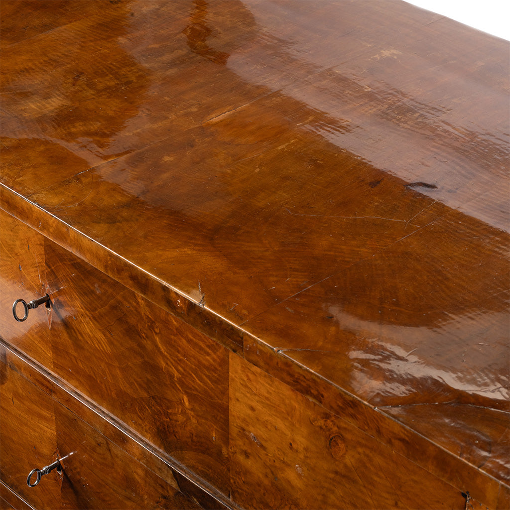 Close-up of a glossy medium-brown wooden chest with visible drawer fronts and small dark metal pulls.