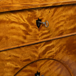 Close-up of a polished wood dresser with a rich golden-brown flamed wood grain finish, featuring a silver keyhole handle and a decorative horizontal wood rail.