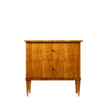 Front view of an antique Biedermeier two-drawer chest featuring a warm honey-colored wood veneer with beautifully matched figured grain across the drawer fronts. Simple diamond-shaped pulls, tapered legs, and clean, elegant lines reflect the refined craftsmanship of the Biedermeier style.