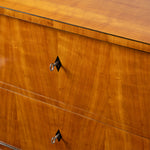 Close-up of a polished wood cabinet or dresser drawer front with warm honey-toned grain, a thin dark edge trim, and silver metal drawer pulls.