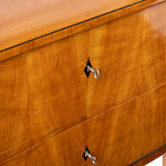 Close-up of a polished wood cabinet or dresser drawer front with warm honey-toned grain, a thin dark edge trim, and silver metal drawer pulls.