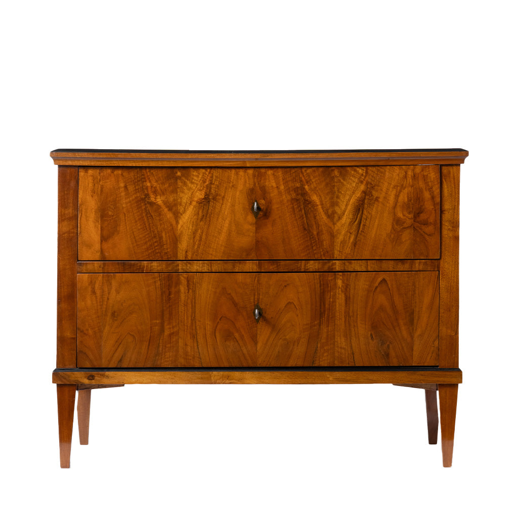 Front view of an antique Biedermeier two-drawer chest featuring striking bookmatched walnut veneer with richly figured wood grain across the drawer fronts. Simple round pulls, tapered legs, and clean, balanced proportions emphasize the piece's refined craftsmanship and elegant design.