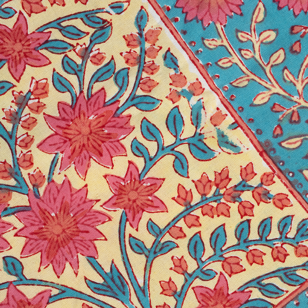 Beige tablecloth corner with pink floral print and blue leafy accents next to vibrant turquoise border with floral motifs.