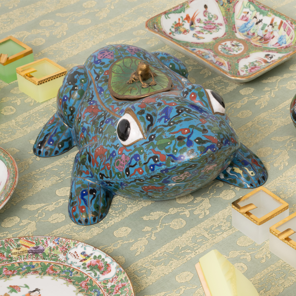 Decorative ceramic frog on a patterned surface with other decorative items.