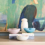 Decorative setup with bowls and a vase on books against an abstract painting background.