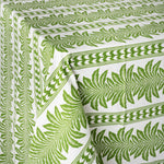 close up image of a green and white tablecloth with palm tree pattern, draped over a table, on a white background