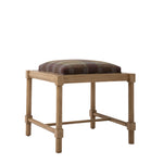 Three-quarter view of the Hank Cocktail Table Ottoman showing the plaid upholstered cushion, natural wood frame, and open base. The wood grain and warm tones complement the multicolored wool plaid.