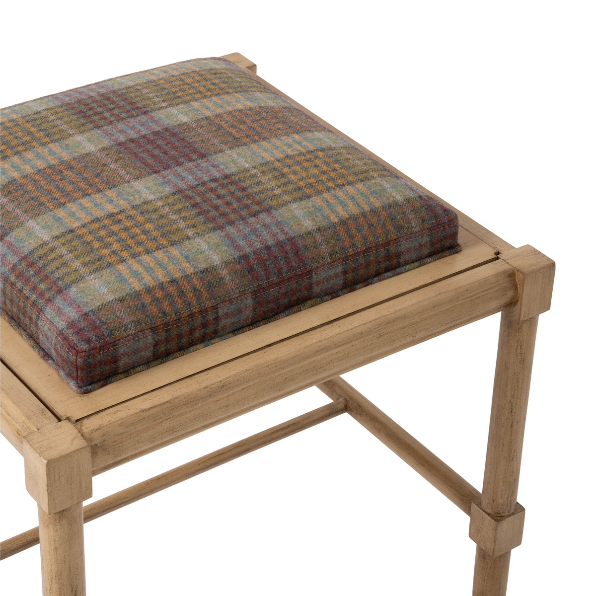 Angled close-up of the Hank Cocktail Table Ottoman highlighting the cushioned wool plaid seat. The upholstery features a warm mix of rust, blue, gold, and muted neutral tones.