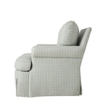 Side profile of the upholstered armchair highlighting its rounded arm, deep cushioned seat, and gently curved back. The skirted base and neutral patterned upholstery create a soft, traditional silhouette.