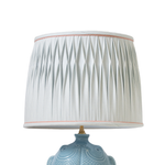 Light blue ceramic lamp with a pleated white lampshade on a white background
