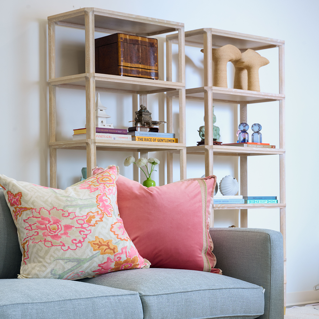 Blue sofa with colorful pillows in front of shelves filled with various decor.