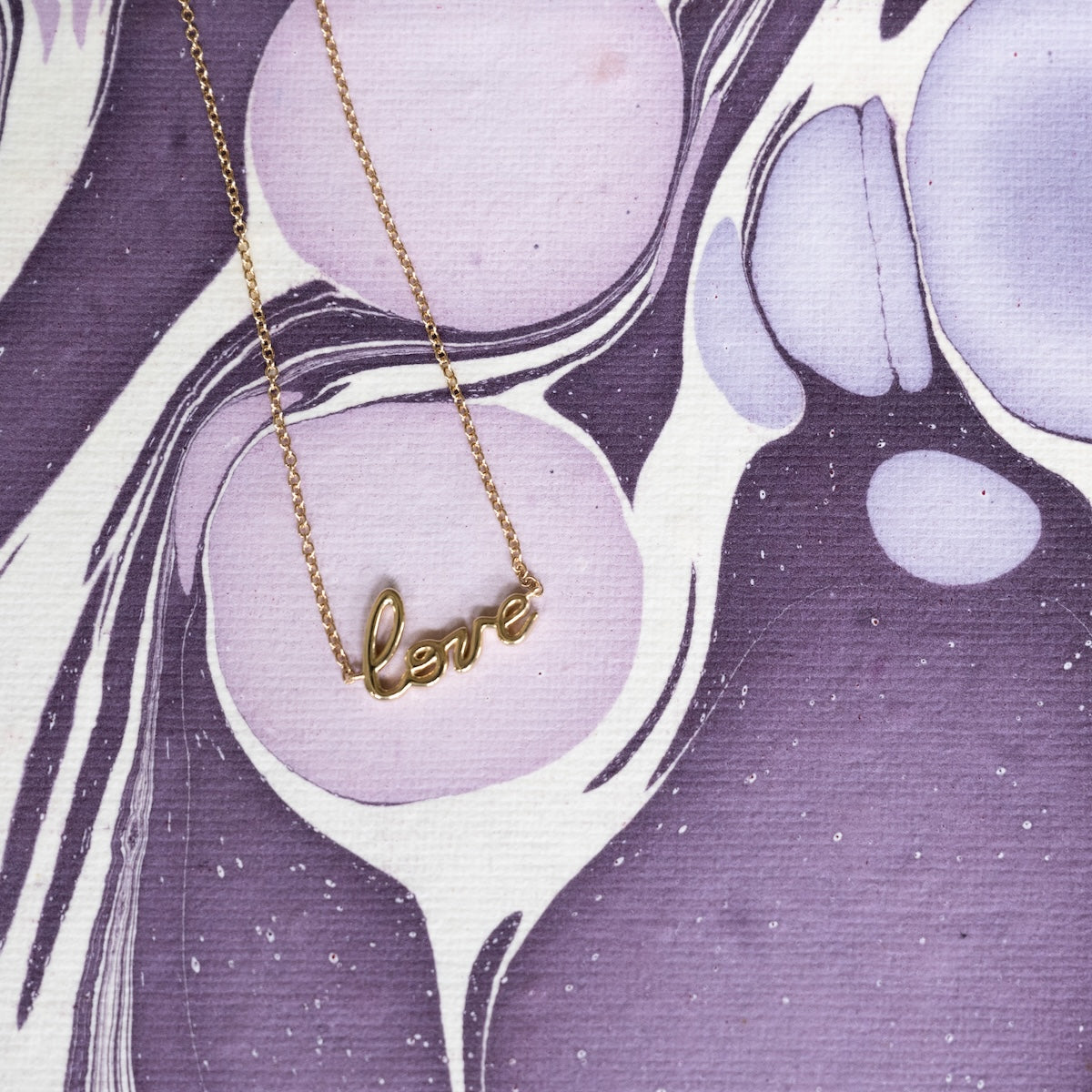 Gold bracelet with 'love' pendant on a purple abstract background