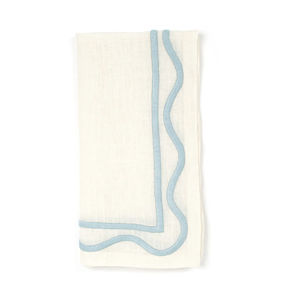 A folded white napkin with light blue squiggle embroidered detailing on the edges.