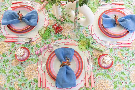 A bring tablescape with green tablecloth, blue napkins, and pink accessories