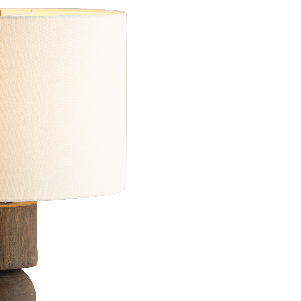 Close-up of a table lamp with a warm white fabric drum shade and a dark wood base, shown against a plain white background.
