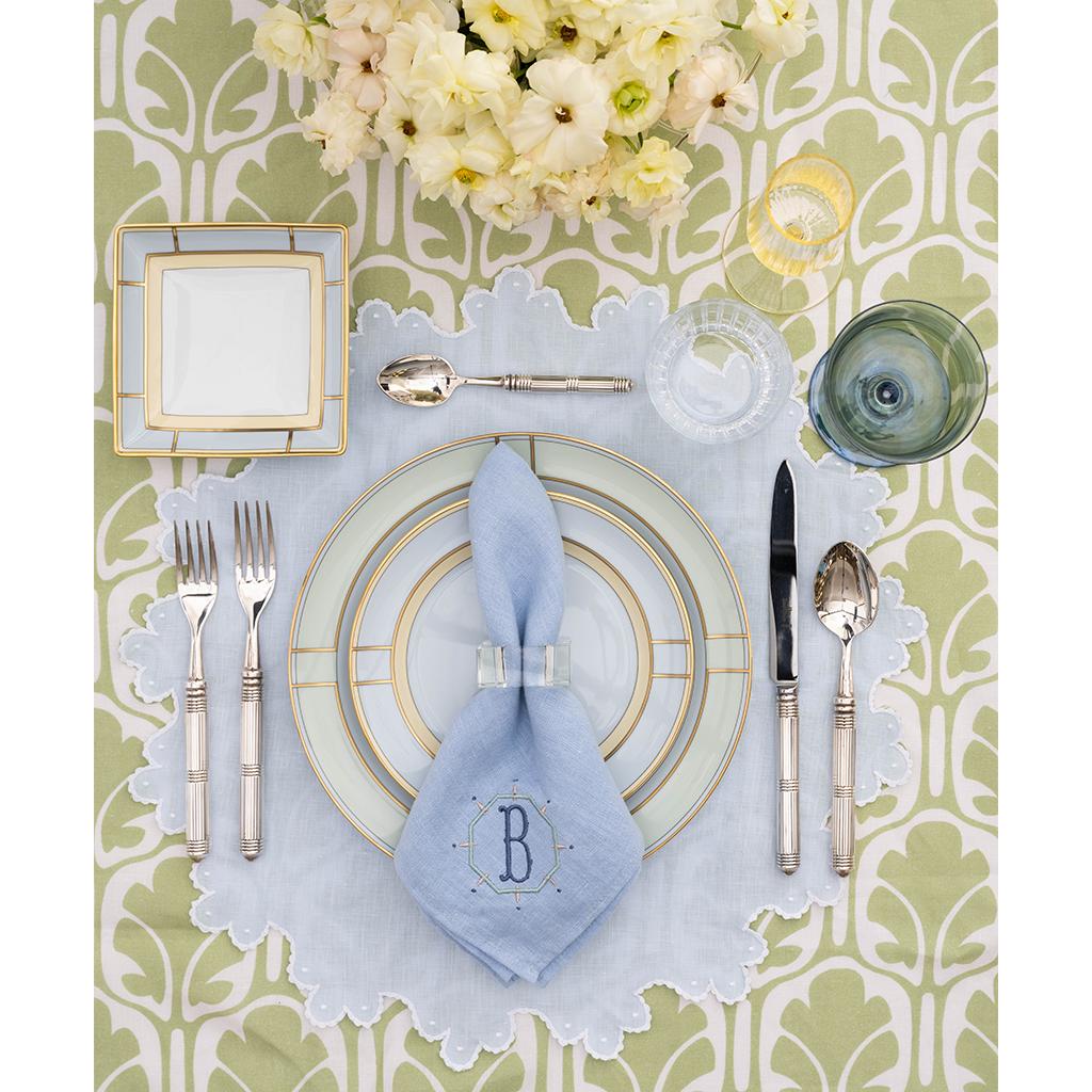 Table-setting with green and white tablecloth, green and blue china, and a monogrammed blue napkin.