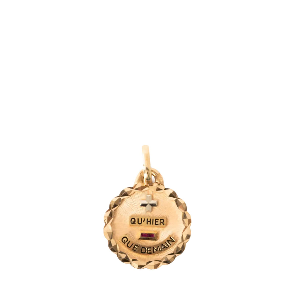 A gold-toned round pendant charm with a faceted textured edge, featuring a small cross at the top, the engraved words 'QU'HIER' and 'QUE DEMAIN' on either side of a small red ruby detail, and a bail at the top for a chain.