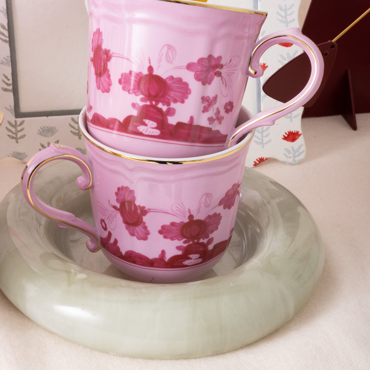 Two pink floral mugs stacked on a green catch all with a blurred background