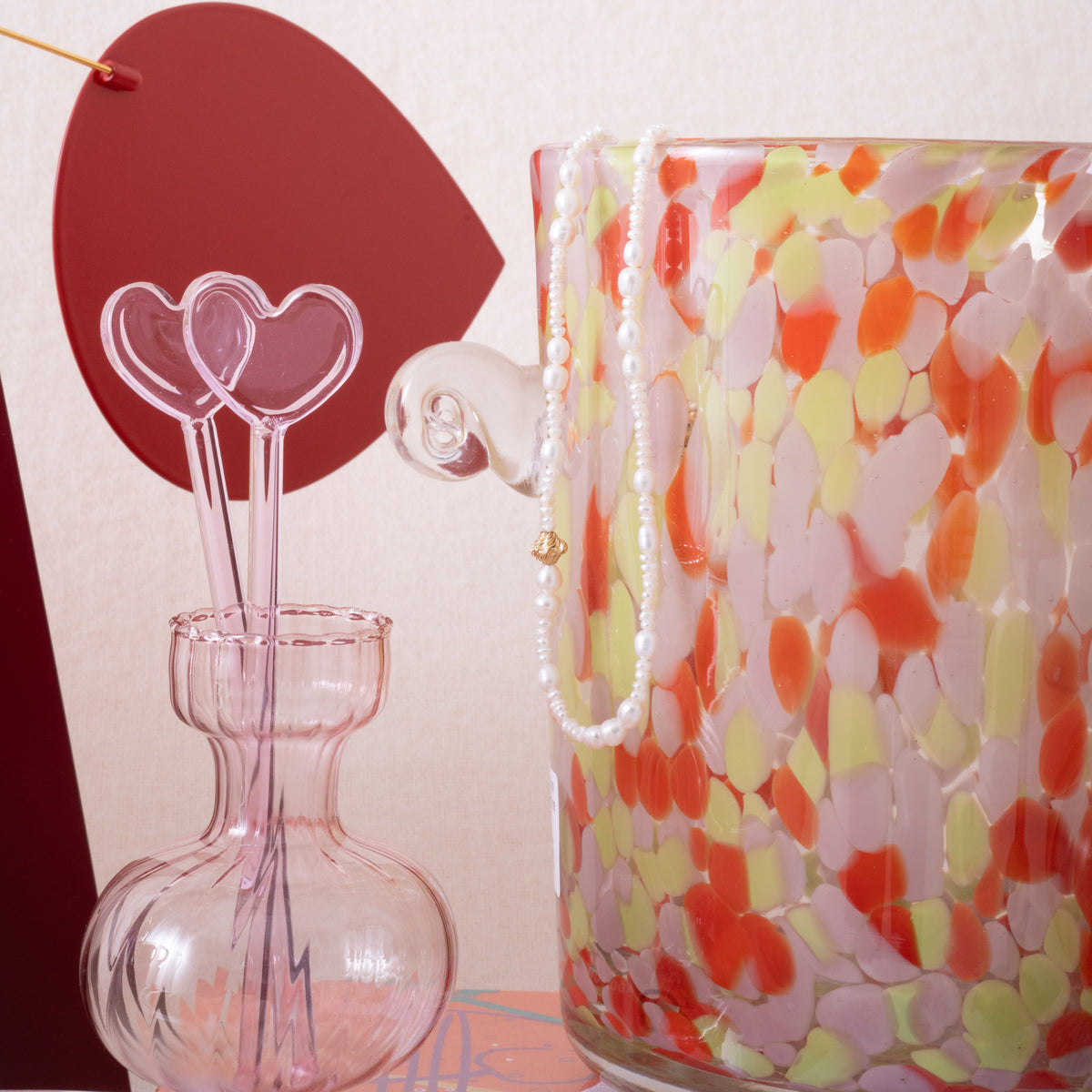 Decorative glass ice bucket with colorful pattern next to a pink hourglass-shaped vase with heart swizzle sticks.