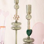 Green candle holders with necklaces on a light pink background