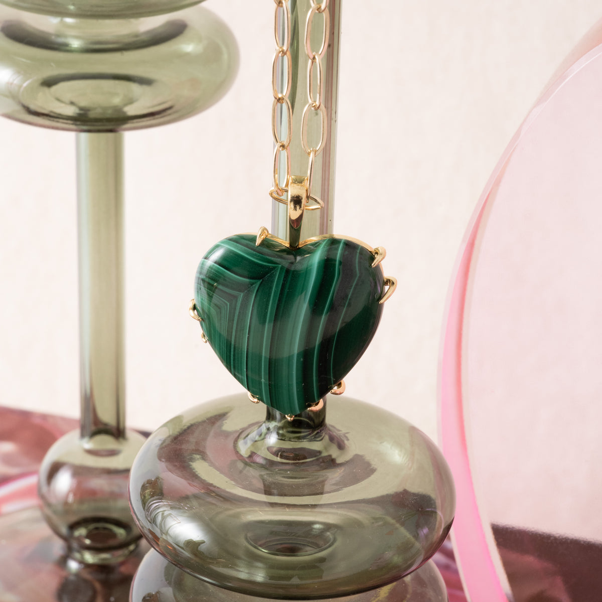 Green heart-shaped pendant on a chain with a glass candle holder in the background
