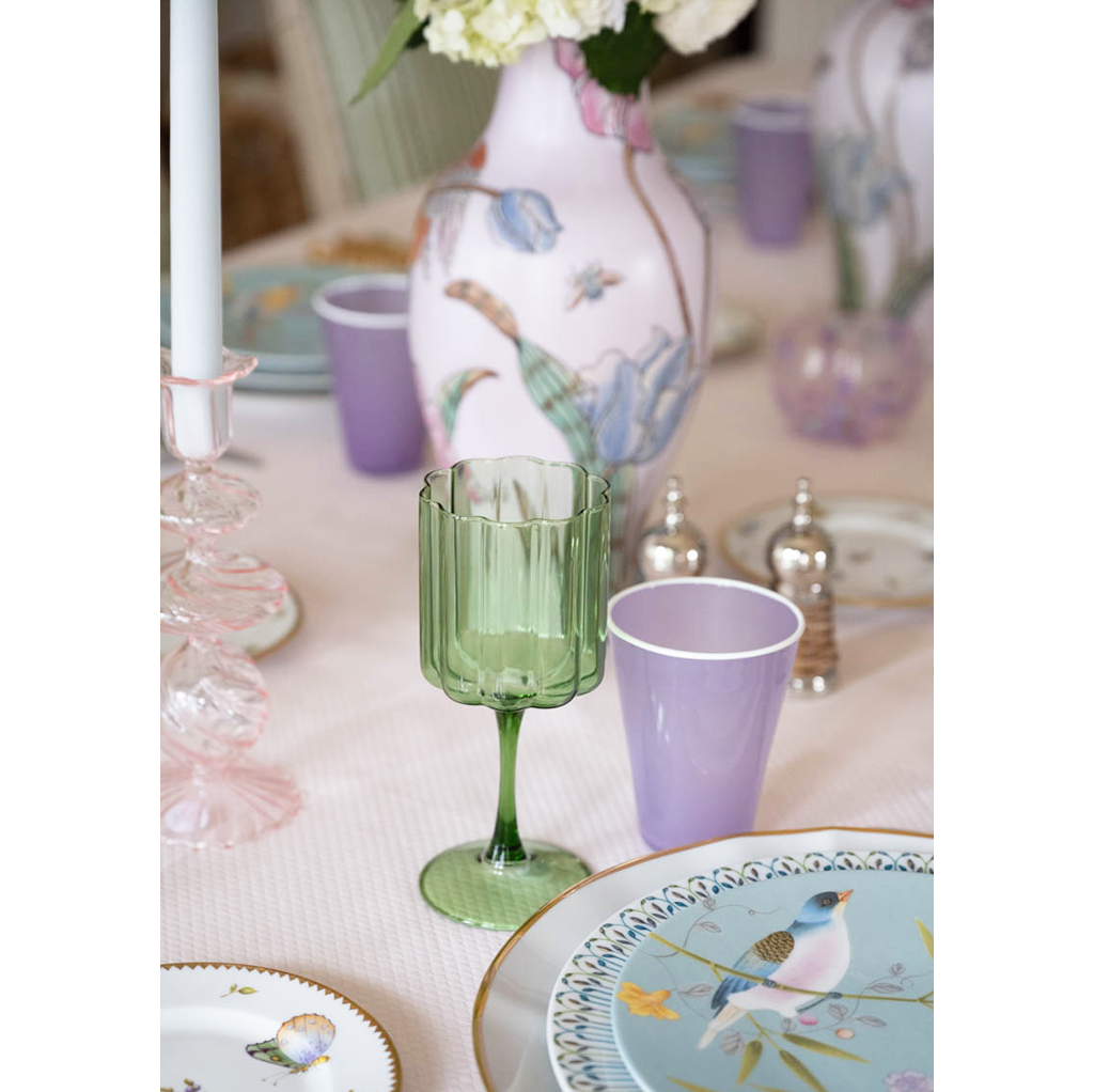 close up of a green scallopedwine glass and purple ceramic water up on a dining table