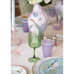 close up of a green scallopedwine glass and purple ceramic water up on a dining table