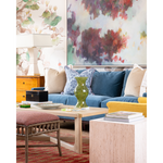A styled living room scene featuring a blue sofa with beige and blue patterned pillows, a yellow accent chair, a light wood coffee table, and a large abstract painting on the wall behind it.