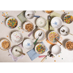 Assorted flatware pieces with horn handles in various colors alongside patterned bowls and scattered cereal on a table.