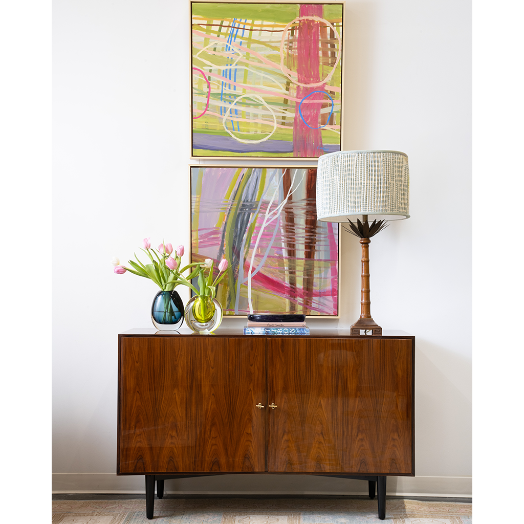 Wooden sideboard with abstract art and decorative items against a white wall.