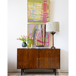 Wooden sideboard with abstract art and decorative items against a white wall.