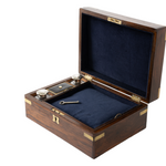 An open wooden presentation box with a dark wood exterior, brass corner and latch accents, and a dark blue velvet-lined interior. A small key and ink containers are placed inside the compartment.