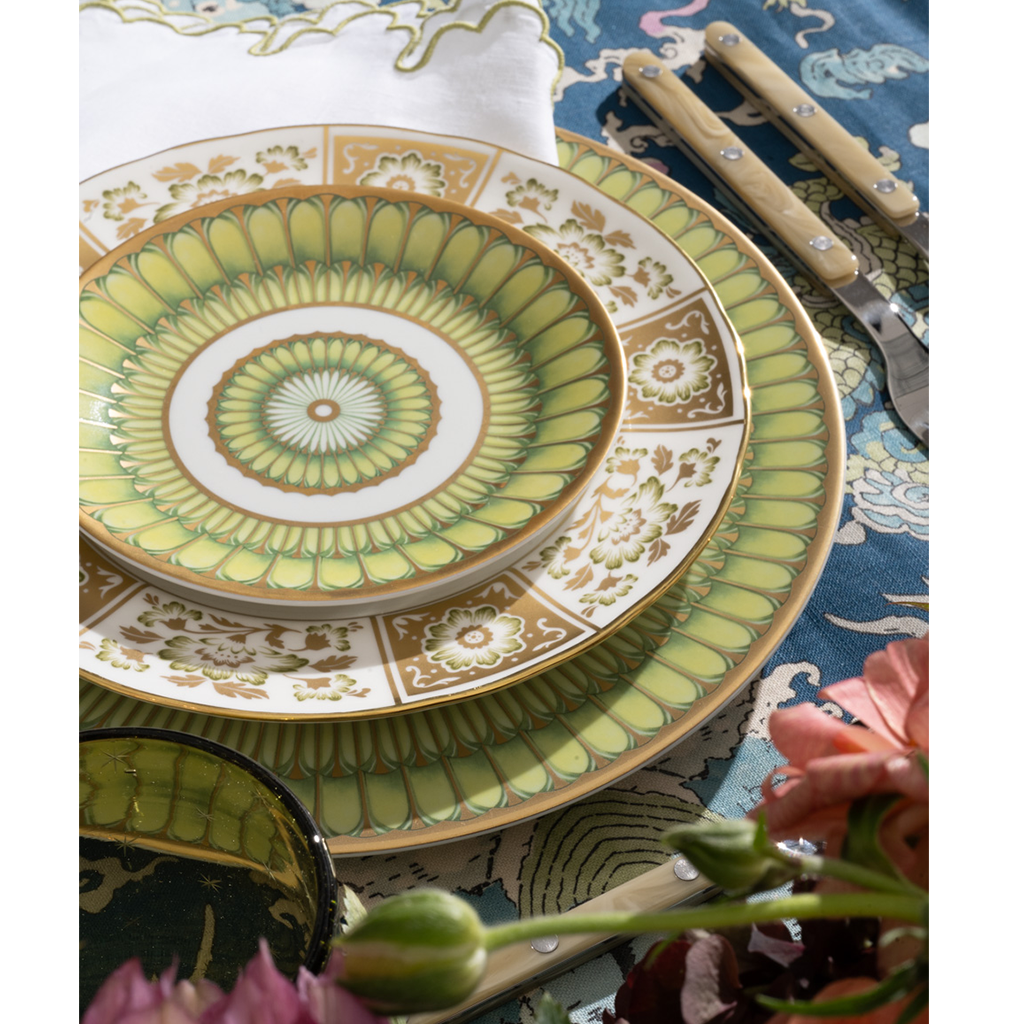 Decorative green and gold plate on a table with flowers and cutlery