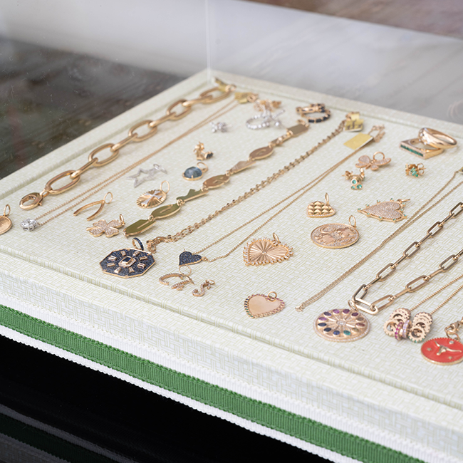 Delicate gold chain bracelet with heart and charm pendants on cream jewelry display.