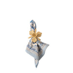 A folded patterned napkin in cream, blue, and white with a gold flower-shaped napkin ring, shown on a plain white background.