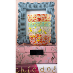 Decorative stack of colorful bowls with a textured blue frame on a pink surface.