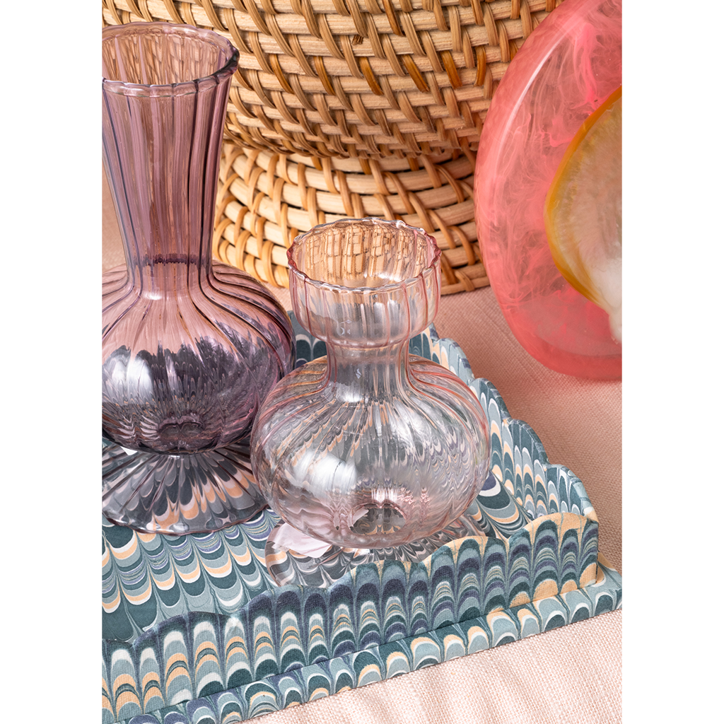Pink glass vase on a decorative tray with a woven basket in the background